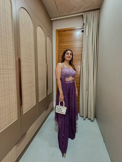 A full-length shot of the purple ruffle saree, styled with a simple white pearl bag. The monochromatic look is slimming, and the ruffles add a playful, dramatic touch.