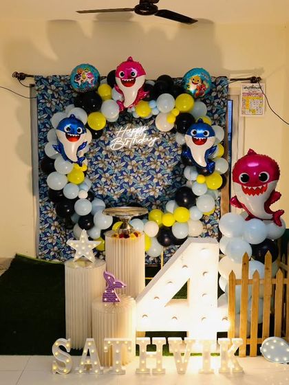 A fun Baby Shark themed birthday decoration set up at home. The design includes character balloons, a printed backdrop, and a light-up marquee number '4'.