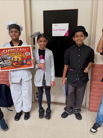 A group of students ready for their Trinity exam, dressed as characters for a fast-food themed play. Their creative costumes and props are a key part of bringing their devised drama piece to life.