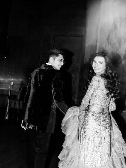 A candid black and white shot of the couple walking away, the bride looking back with a smile, creating a playful and romantic image.