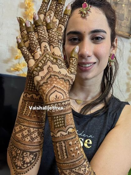 A happy bride showing off her intricate back-hand mehndi. The design is dense with traditional patterns, creating a beautiful and complete bridal look.