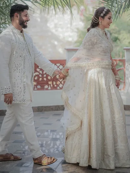 The groom leads his bride, her hand in his, through a palace courtyard. This shot captures a sense of journey and togetherness, framed by the beautiful architecture and natural light.
