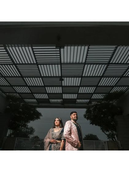 A dramatic, low-angle shot of a couple standing under a modern geometric pergola, creating a powerful and stylish portrait.
