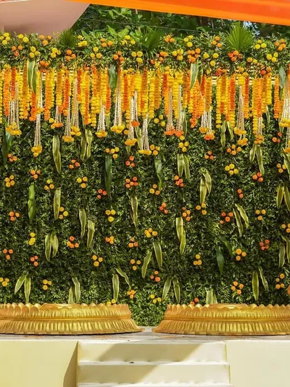 A stunning Haldi stage with a backdrop made entirely of green leaves and decorated with hanging marigold strings. The golden temple-style props add a divine touch.