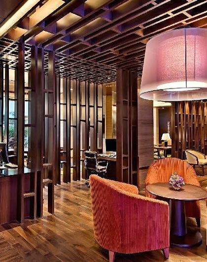 A seating area in the Sheraton lobby, showcasing a mix of textures and colors. The vertical wooden slats create a visual screen while maintaining an open feel, complemented by plush orange armchairs.
