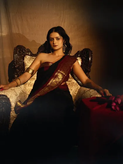 A painterly portrait with a vintage feel, inspired by classic art. The model is seated on a throne-like chair, draped in a traditional saree, exuding quiet authority.