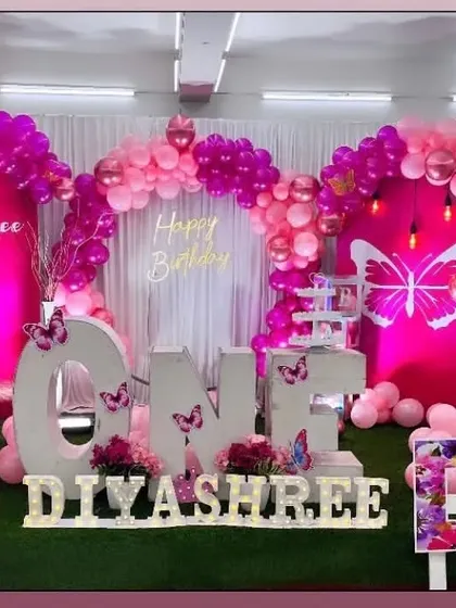 A vibrant magenta butterfly theme for a first birthday. This striking setup uses large 'ONE' letters as a central feature on a grass floor.