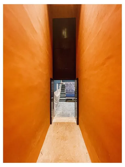 A narrow, compressed passageway with vibrant orange walls opens into a larger space, creating a dramatic sense of arrival. I use such spatial sequences to guide movement and shape the emotional experience of moving through a building.