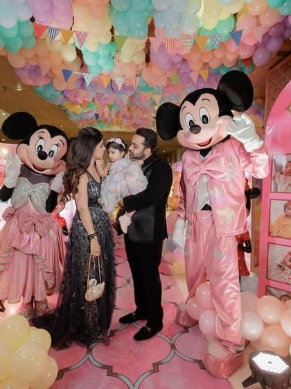 The birthday girl and her parents posing with Mickey and Minnie Mouse mascots in front of the photo display wall.