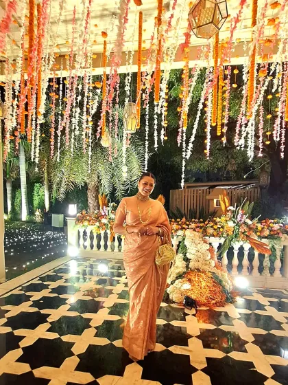 Attending a wedding celebration in a timeless peach-toned saree. The simplicity of the drape is elevated by a classic pearl necklace and a handcrafted bag, proving that elegance often lies in understated details.