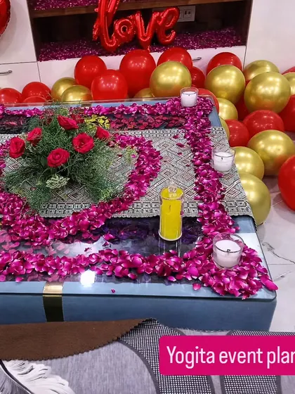 A close-up of the detailed table decoration for an anniversary. I use fresh rose petals to create a border around a floral centerpiece, surrounded by candles for a warm and intimate feel.