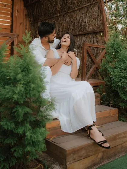 A moment of pure, uninhibited laughter on a rustic wooden porch. Dressed in coordinated white, this couple's joy is infectious, showcasing a perfectly candid moment from their pre-wedding shoot.