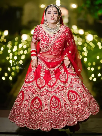 A fun and playful bridal portrait. The bride, in her vibrant red lehenga, makes a cute pout for the camera against a backdrop of twinkling lights, showing her fun personality.