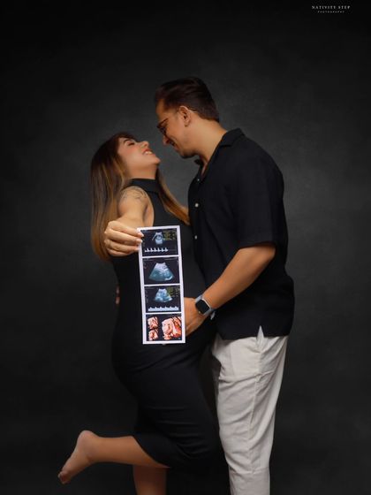 A joyful and playful couple's portrait, celebrating with their ultrasound scan. Her fun pose and their happy expressions are infectious.