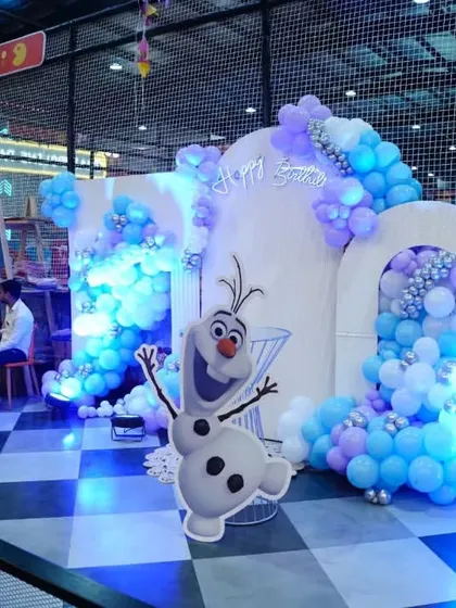 A wide view of a 'Frozen' party setup, with a beautiful white arch, character cutouts, and blue lighting to create an icy, magical ambiance.