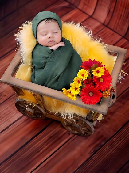 A newborn rests in a charming little wooden cart. The combination of the rustic wood, soft yellow fur, and colorful flowers creates a vibrant and cheerful image.