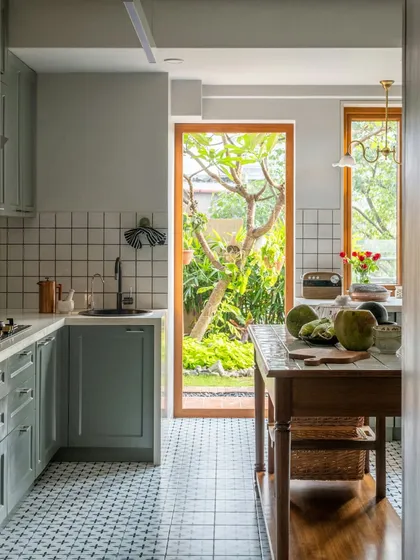 A view from the kitchen into the garden of a Calcutta home. The layout is designed to be open and airy, with a tiled island that serves as a workspace and a casual spot for a morning coffee. It’s a kitchen that feels connected to nature.