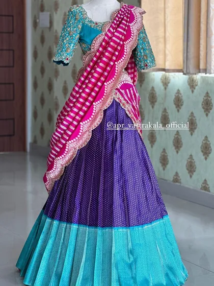 This bridal half-saree set is a masterpiece of color and texture. The design combines a pleated turquoise and purple brocade skirt with a heavily embroidered turquoise blouse and a contrasting striped pink dupatta for a bold, modern bridal look.