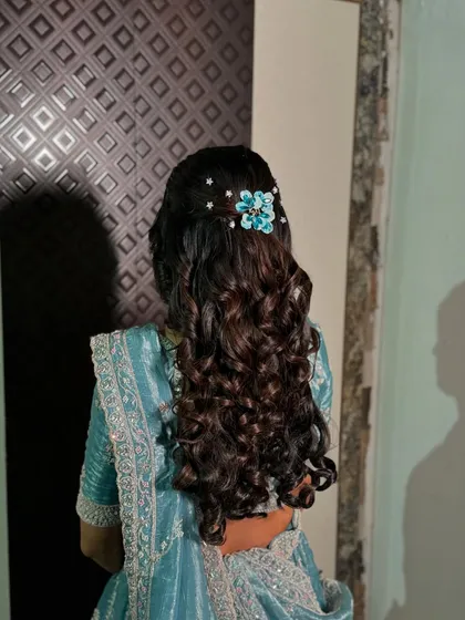 A beautiful half-updo with voluminous curls, decorated with a floral hair clip for an engagement.