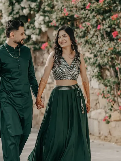 The couple enjoys a relaxed walk, holding hands and sharing a smile. Dressed in elegant dark green outfits for their Mehendi, this candid shot captures a moment of simple happiness.