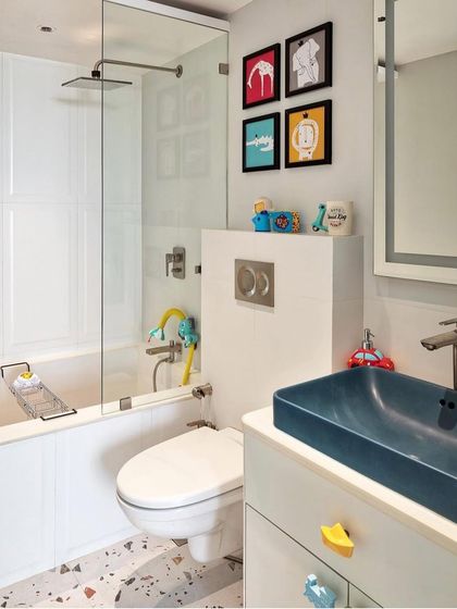 A fun kid's bathroom with a clean, modern design. The space features a deep blue sink, playful drawer pulls, and colorful framed art above the toilet.