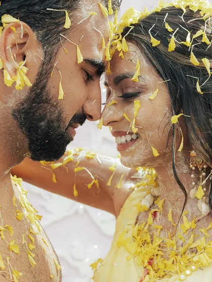 An intimate close-up of the couple, their faces adorned with turmeric and flower petals, sharing a moment of pure love and happiness.