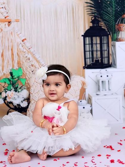 A baby girl in a fluffy white dress sits in a dry tub, surrounded by rose petals and boho decor. This is a great option for capturing the theme without the water.