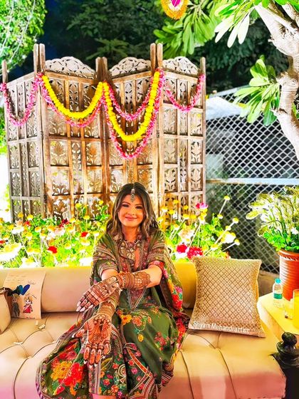 A happy bride posing at her vibrant mehandi ceremony, her intricate henna on full display.