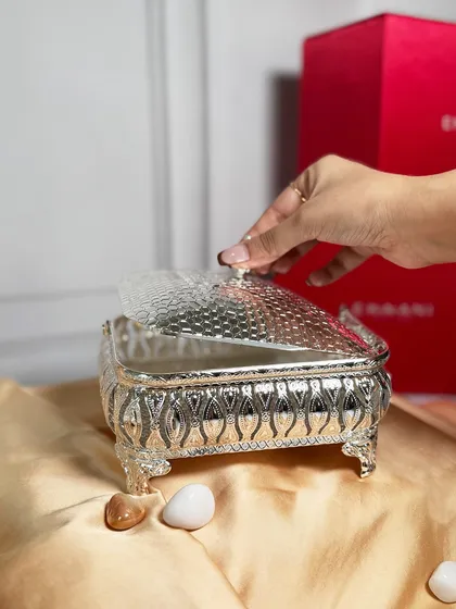 A hand lifts the lid of a rectangular silver basket, revealing its potential for holding gifts or treats. The hammered texture of the lid adds a touch of artisanal beauty.