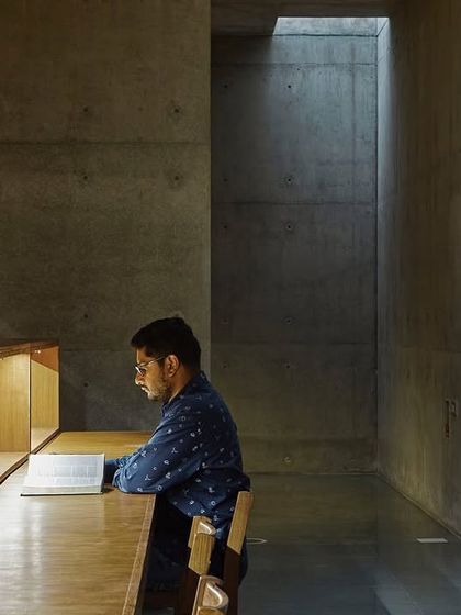 A quiet study carrel at the Lilavati Lalbhai Library, carved into a niche of wood and concrete. A narrow skylight washes the raw concrete wall with natural light, creating a serene and contemplative space for individual work.