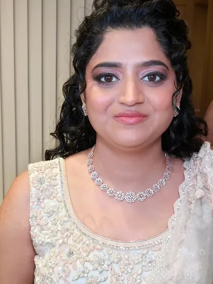 This bride's reception look is all about soft elegance. Her naturally curly hair is styled in a beautiful half-updo with a delicate accessory, and the makeup is kept soft and luminous.