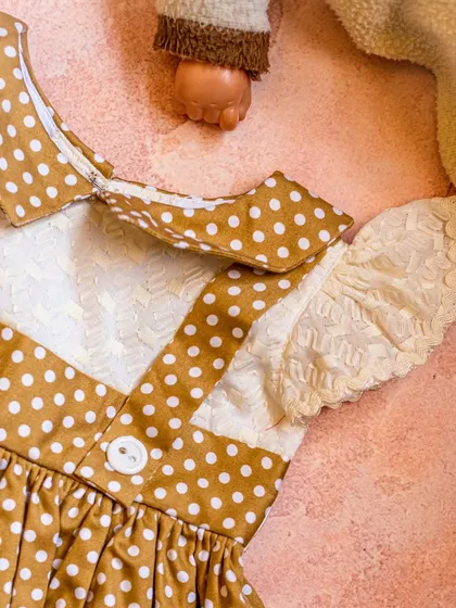 A close-up of this charming mustard polka dot dress. The design features lace-trimmed flutter sleeves and a classic collar for a vintage-inspired feel.