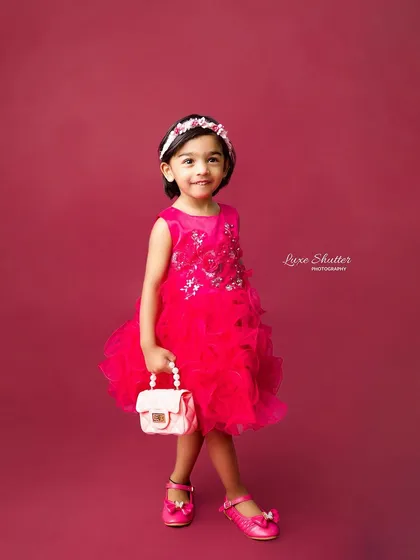 A sweet, smiling portrait of a little girl in a vibrant pink dress against a matching backdrop. Simple, classic, and beautiful.
