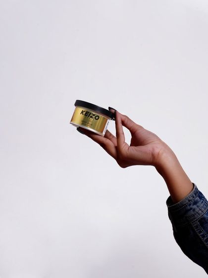 A minimalist shot of a hand holding the "Keizo Gold" grooming product, clean and straight to the point.