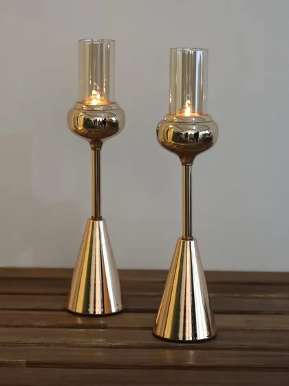 A pair of our tall Vesper candle holders, their golden finish glowing warmly. These are designed to add height, drama, and a sophisticated ambiance to any room.