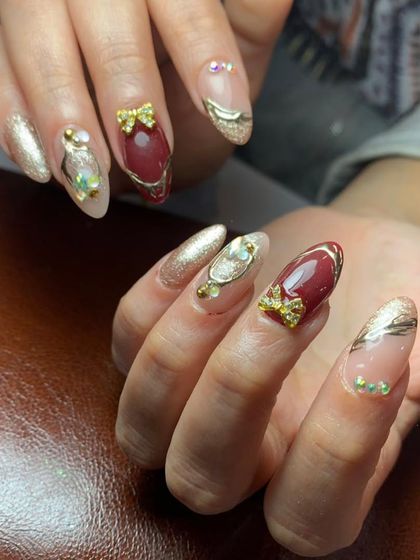 An elegant combination of deep red and gold chrome nails, with accent nails featuring 3D gold bows and crystal details.