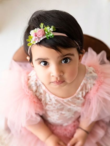 An overhead shot of a baby girl in a pink dress, looking directly into the camera with her big, expressive eyes.
