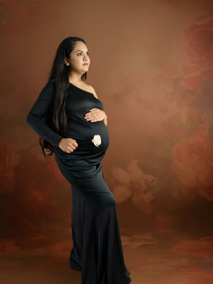 A powerful and elegant solo portrait of a mom-to-be in a black one-shoulder gown against a textured, artistic backdrop.