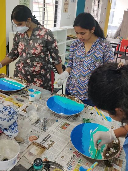 A group of women working on their resin art pieces, carefully adding shells and creating beautiful blue waves.