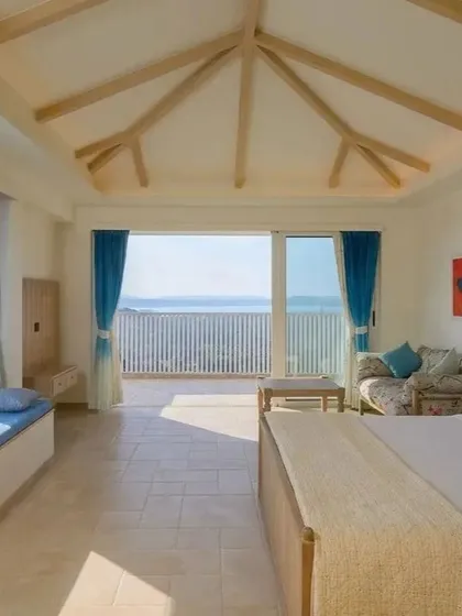 This spacious bedroom features an exposed beam vaulted ceiling and large sliding doors that open to a balcony. The design maximizes the sense of space and connection to the outdoors, with a built-in window seat for enjoying the view.
