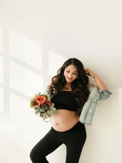 A pop of color from a fresh bouquet adds a lovely touch to this casual maternity portrait. The mom to be looks so happy and radiant against the simple white wall.