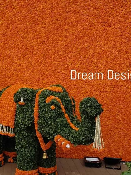 A grand statement piece for a traditional Indian wedding event. This life-sized elephant is meticulously crafted from green foliage and orange marigolds, standing proudly against a full wall of marigold flowers.