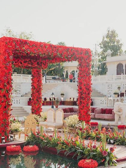 A closer look at the all-red floral mandap, set within the iconic Hathi Kund. The sheer density of crimson flowers creates a powerful statement of love and passion, contrasting beautifully with the serene water and white palace architecture.