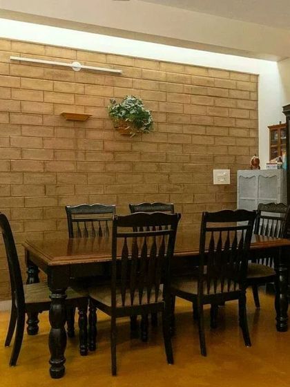 The dining area, with a simple wooden table set against an exposed mud block wall, creating a warm and rustic atmosphere for family meals.