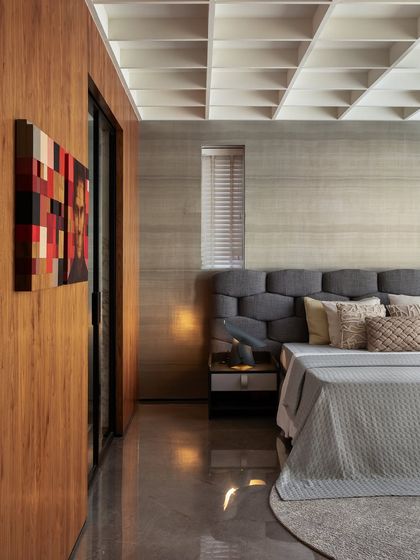 This master bedroom exudes sophistication with its rich wood tones and coffered ceiling. The tufted grey headboard and colorful artwork add layers of texture and personality, creating a perfect mix of comfort and style.