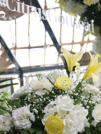 A close up of the "Citrus Got Real" mirror decor. The reflection shows the bright and airy venue, while the foreground highlights the fresh yellow lilies, white carnations, and lemon slice accents.