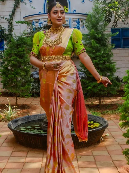 A model in a beautiful peach and green saree, wearing a full bridal set that is also perfect for attending a family wedding.