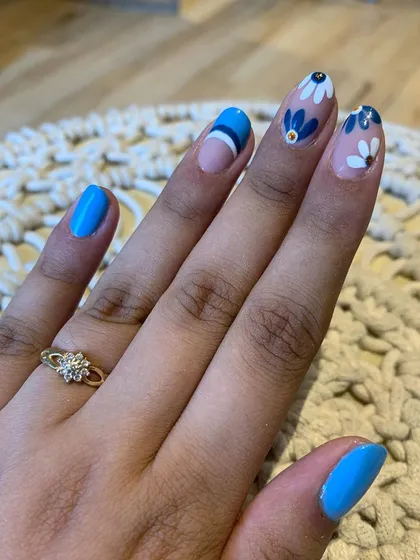 Floral love with a pop of blue. This design combines solid blue nails with accent nails featuring hand-painted daisies and modern stripes.