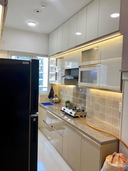 A wide shot of a parallel kitchen with beige high-gloss cabinets and a black refrigerator, showing a clean and organized space.