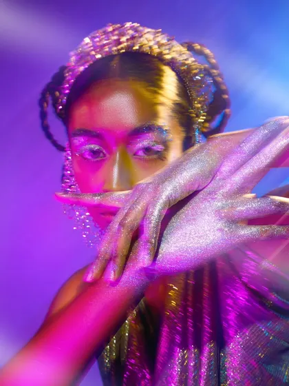 This image from the glitter series uses the model's hands to frame her face, drawing attention to the sparkling makeup and the ethereal lighting. The motion blur adds to the dynamic feel.